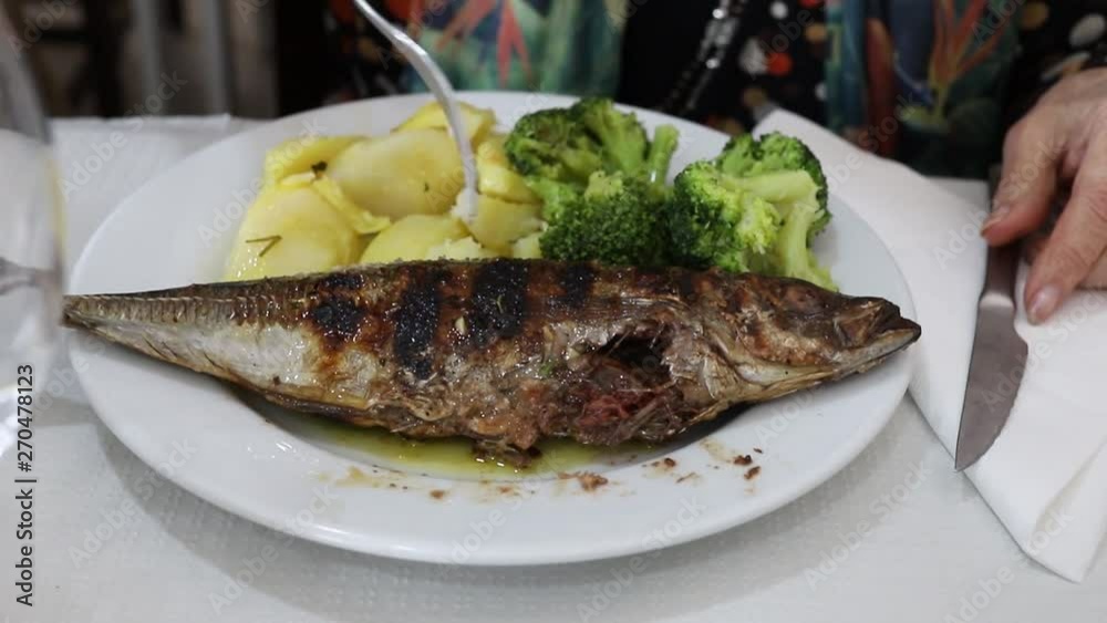 woman eating grilled fish with vegetables on white plate