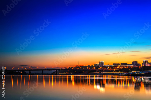 Belsky bridge over the river after sunset at night in the bright orange lights of the city with reflection in the water and a clean colorful blue sky at dusk. White river, Ufa, Bashkortostan, Russia. © Valery Bocman