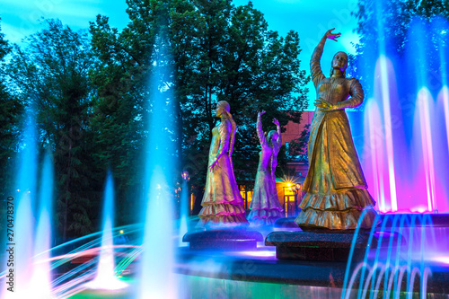 Sculptures of beautiful girls in national dresses in a multi-colored highlight against the background of the night evening sky. Seven Girls Fountain, Ufa, Bashkortostan, Russia - June 2015.