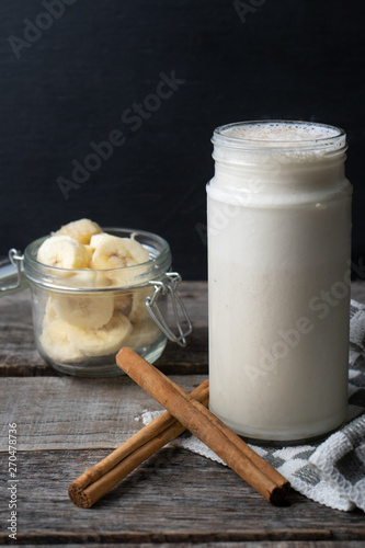 Banana smothie or milkshake with cinnamon on wood background