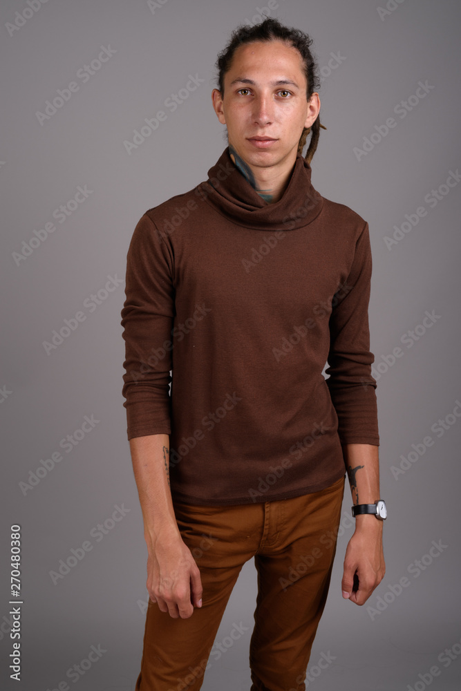 Fototapeta premium Young man with dreadlocks wearing brown shirt against gray backg
