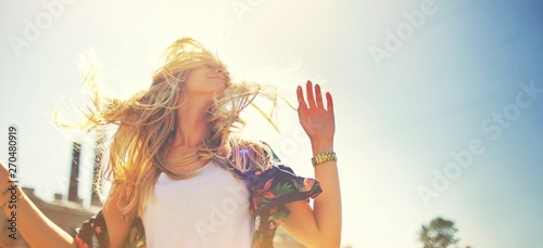 Attractive happy young woman in white t shirt flying hair enjoying her free time at sunset outdoor. Beauty blonde girl portrait at summer. Freedom lifestyle springtime concept. Sun glow on background.