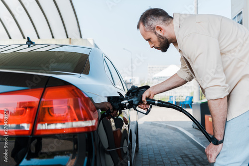 bearded man holding fuel pump and refueling black car at gas station © LIGHTFIELD STUDIOS