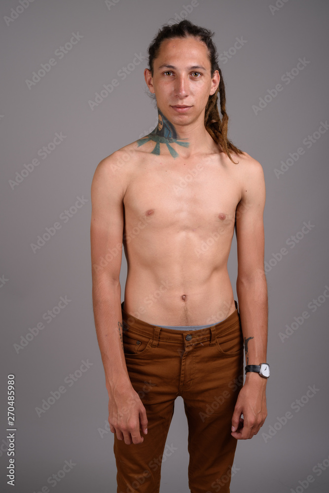 Young shirtless man with dreadlocks against gray background 