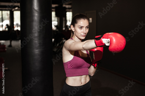 Young pretty woman in red boxing gloves on a background of the gym. Female boxer. Close up portrait of fighter girl. Winner. © Anton Gepolov
