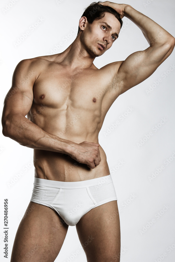 Portrait of handsome young man with stylish haircut in white underwear posing over gray background. Perfect hair & skin. Close up. Studio shot