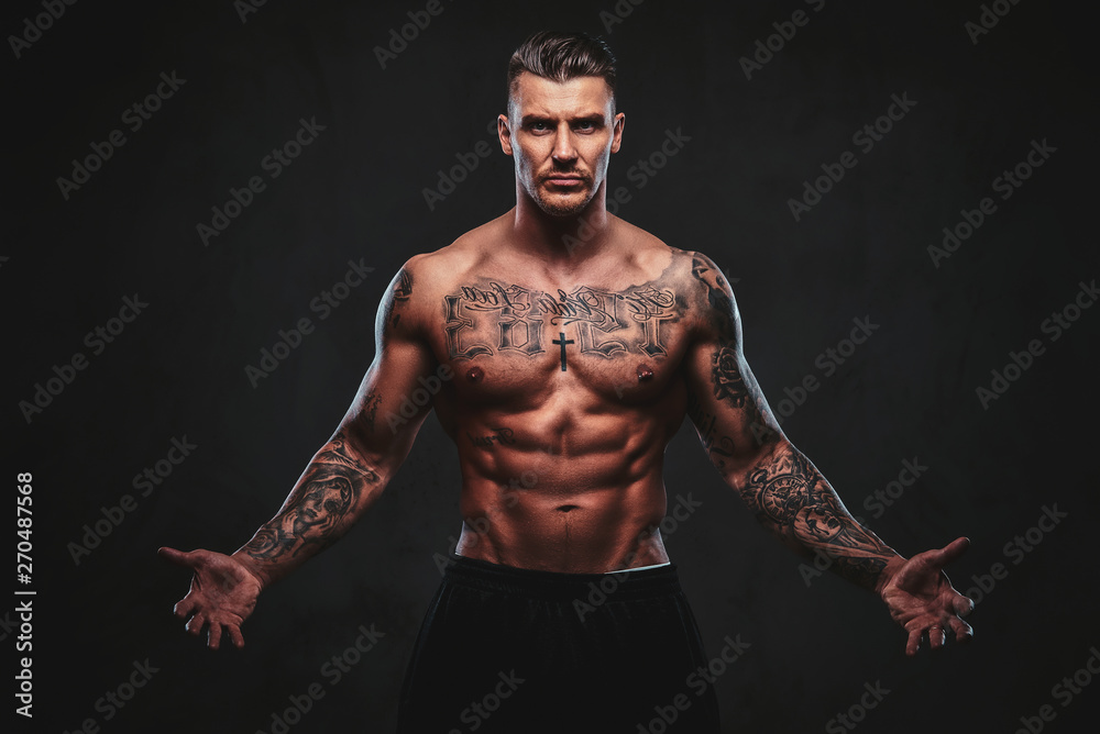 A tattooed muscular shirtless man with stylish hair posing at the camera on a dark background. A tattooed muscular shirtless man with stylish hair posing at the camera on a dark background.