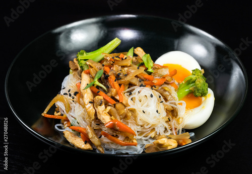 Canvas Print Asian noodles with vegetables and meat on a black background.