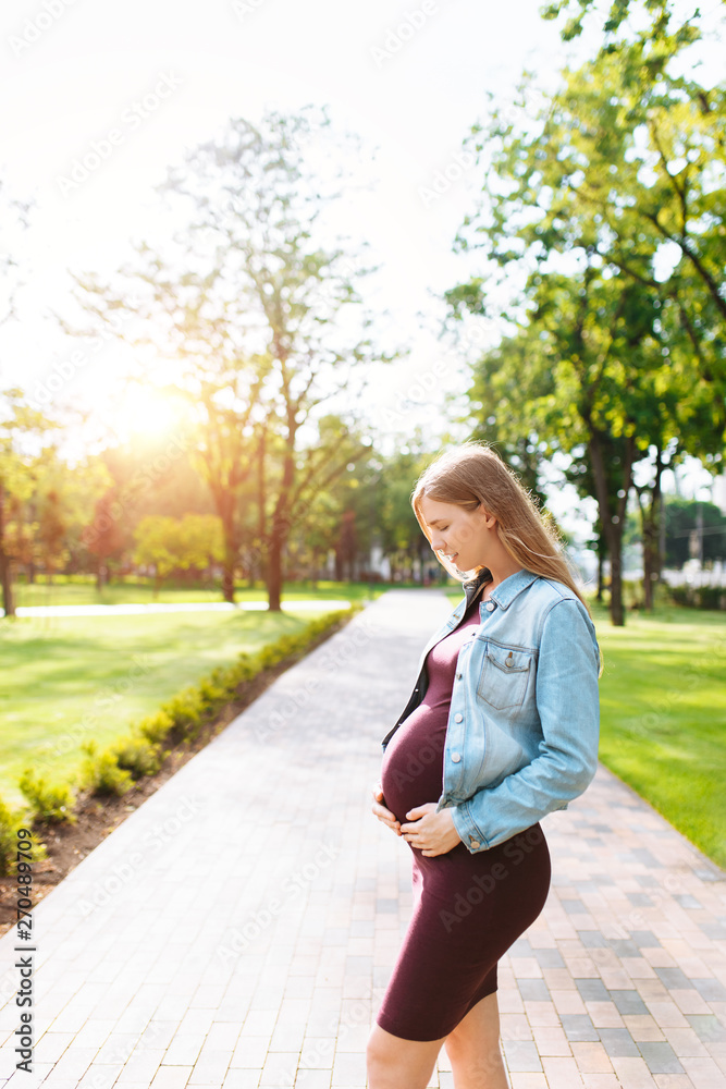 Happy pregnant girl is hugging her belly while walking in the park Happy pregnant girl is hugging her belly while walking in the park