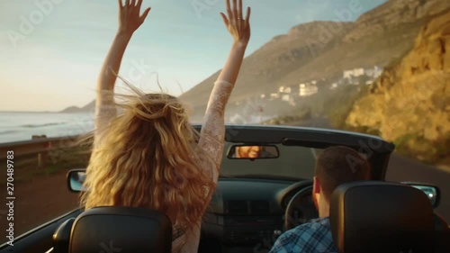 Couple on road trip with convertible driving along coast at sunset photo