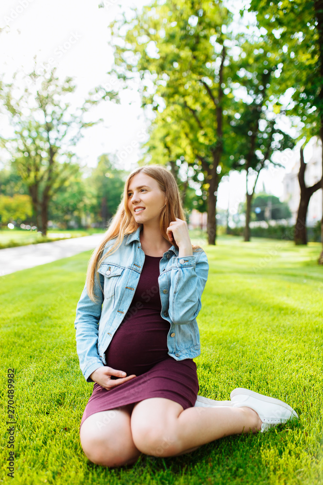 Happy young pregnant woman sitting in the park on the lawn, Happy young pregnant woman sitting in the park on the lawn,