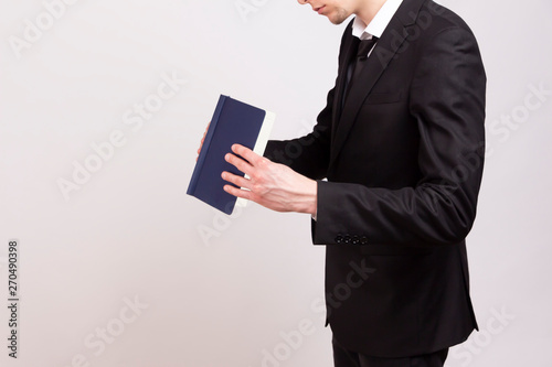 A young man in a black jacket, white shirt and black tie is looking for something in a notebook