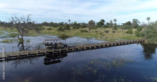 Aerial view of a safari vehicle crossing water on a pole bridge in the Okavango Delta photo