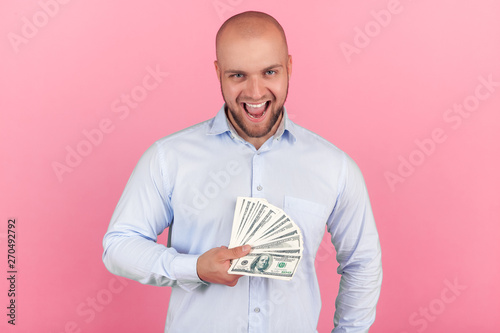 Portrait of a beautiful bald man with a beard dressed in a white shirt. won the lottery happily screming and keeps a packet of money in his hands standing opposite the pink background photo