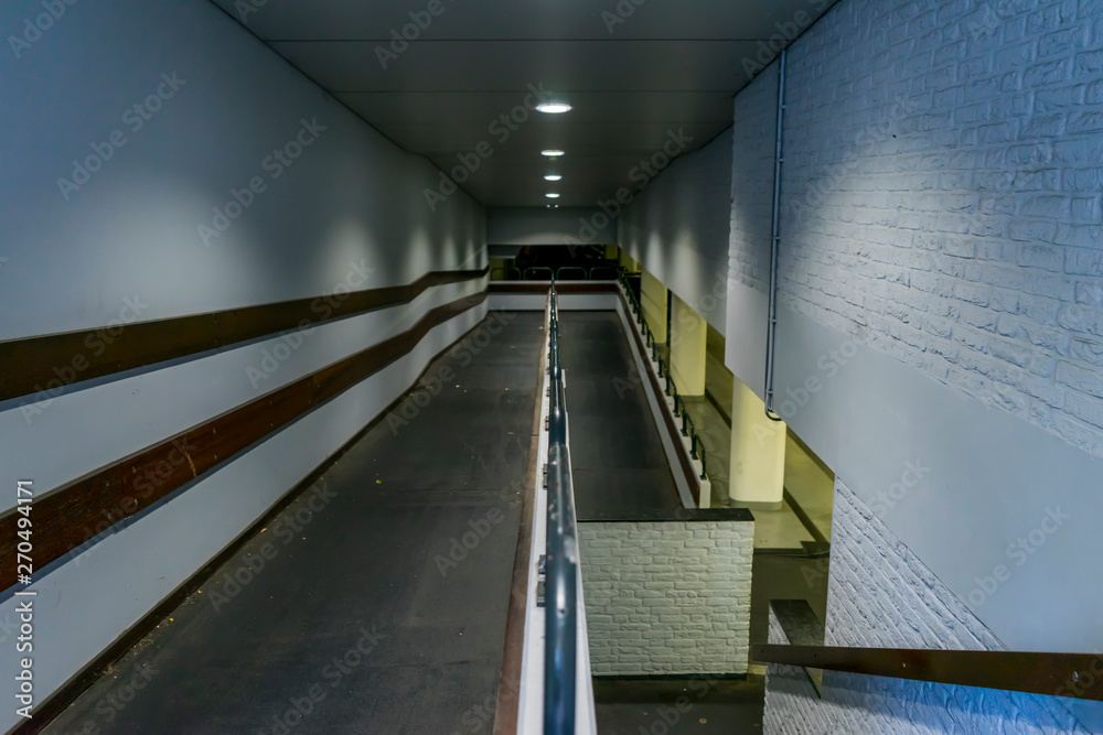 Fototapeta premium Empty walkway down to parking garage. White lamps, white walls and bricks. Stairs down.