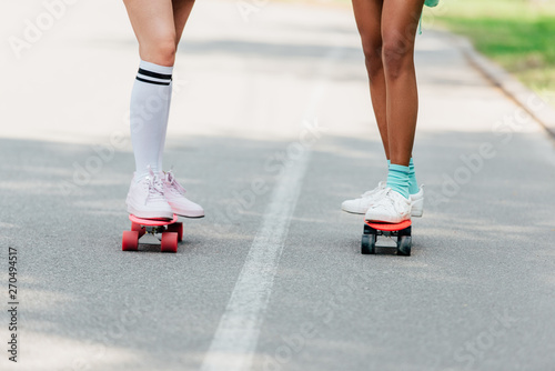 partial view of two girls skateboarding on penny boards on road
