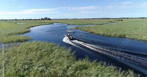 Aerial back view of a tourist boat making its way down one of the many curving waterways of the Okavango Delta photo