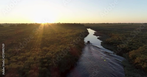 Aerial backlit view of a tourist boat making its way down one of the many curving waterways of the Okavango Delta at sunset photo