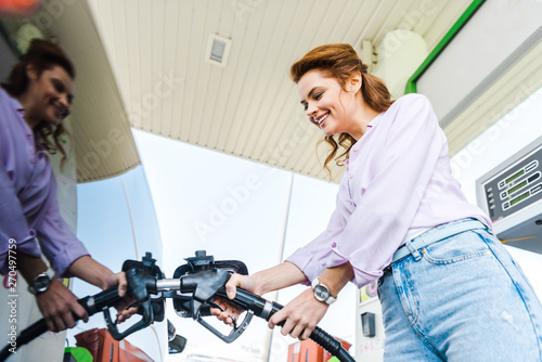 low angle view of happy woman holding fuel pump while refueling car with benzine photo