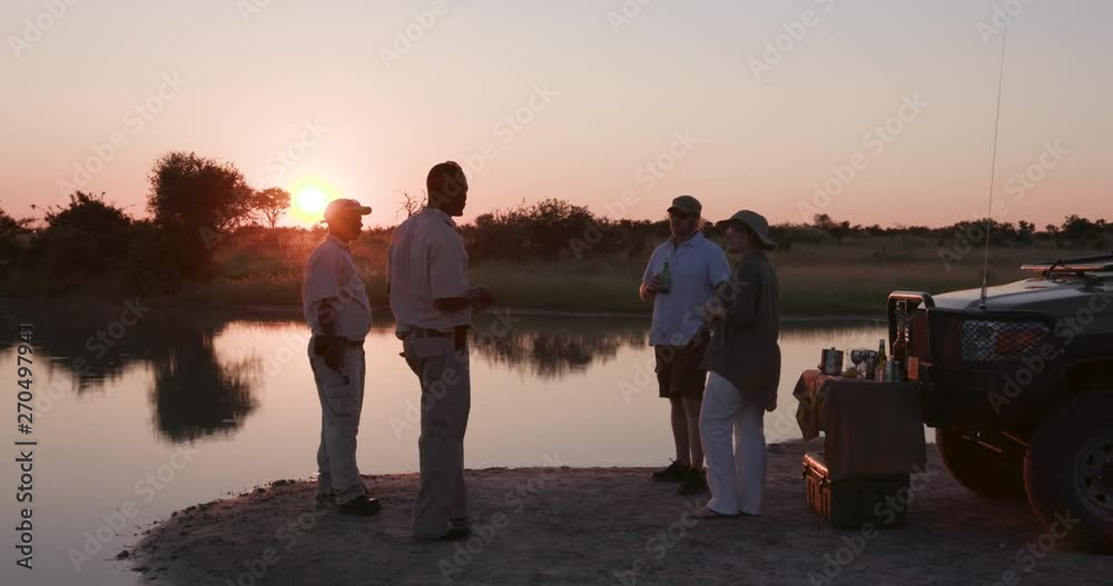 Tourists and guides enjoying a sundowner at the rivers edge in the Okavango Delta at sunset
