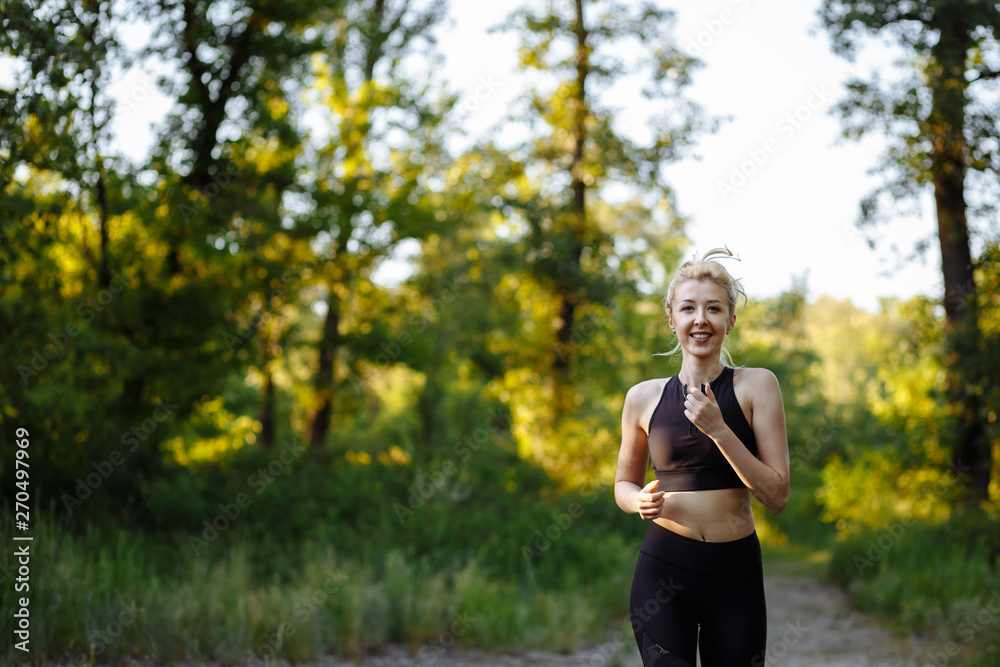 Sports motivation. Young millennial woman in black sportswear running in empty park at the sunset, panorama with free space