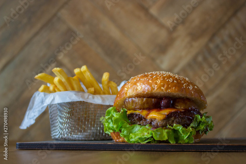 Craft beef burger with pear and cherry and french fries in basket on wooden table isolated on wood wall background.