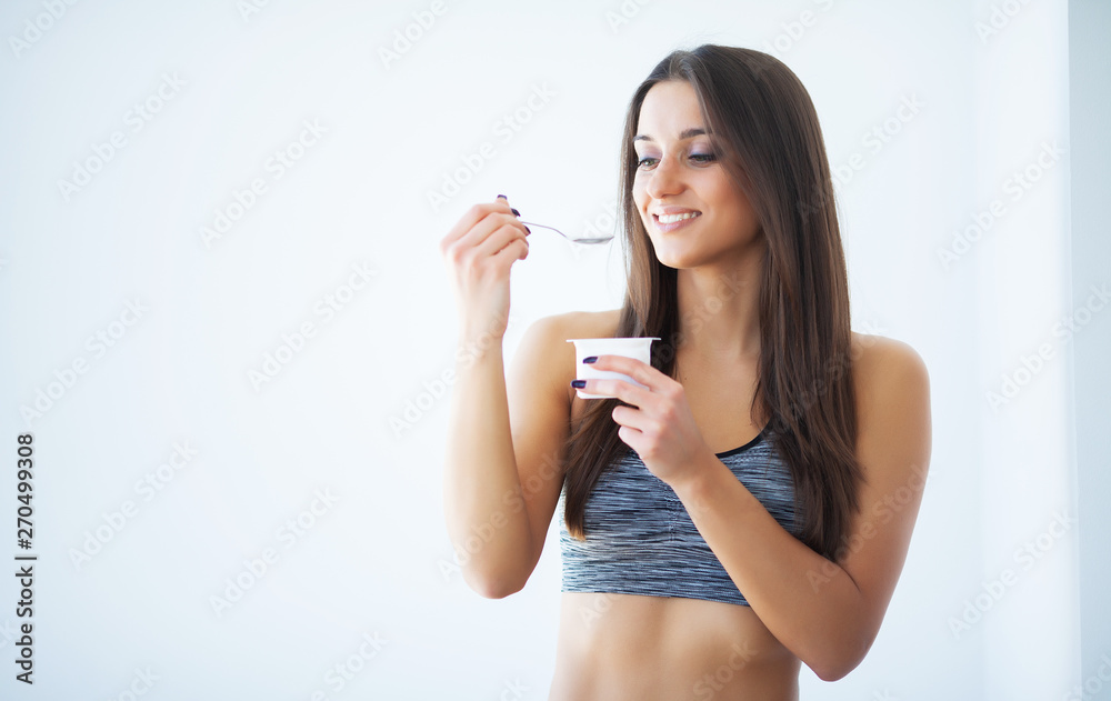 Diet. Happy young woman eating yogurt in kitchen