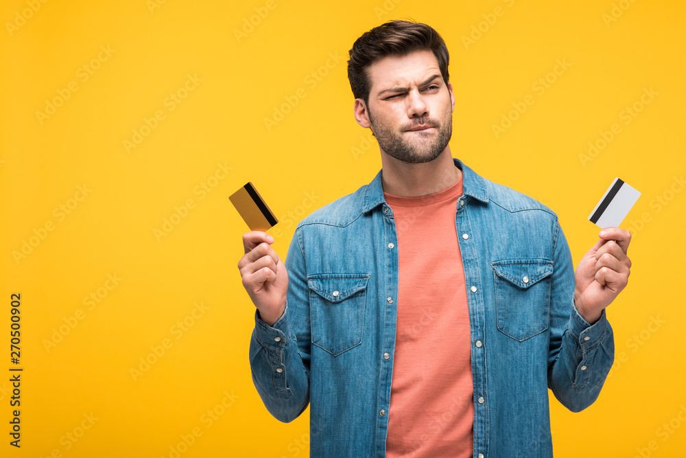 confused handsome man holding credit cards isolated on yellow