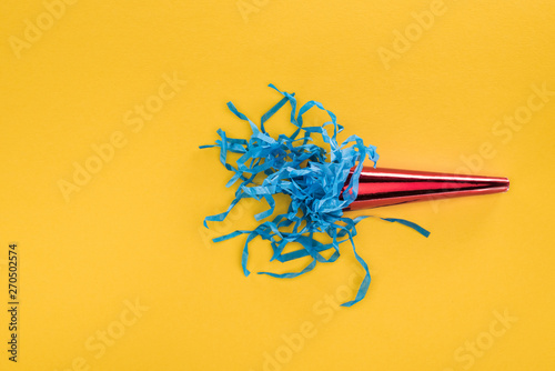 Top view of red party horn with blue paper confetti on yellow background photo