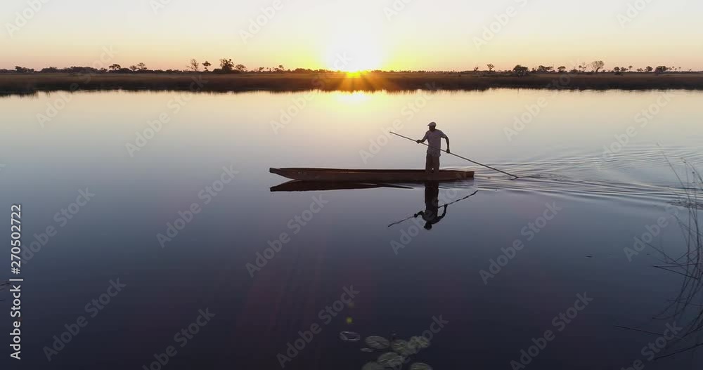 Aerial close-up view of one poler rowing a Mokoro on the waterways of the Okavango Delta at sunset Aerial close-up view of one poler rowing a Mokoro on the waterways of the Okavango Delta at sunset