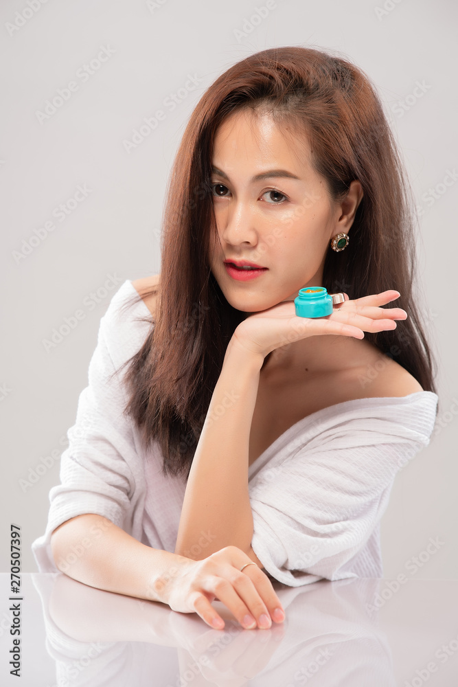 Portrait of asian beautiful woman presenting face cream in studio on grey background; perfection rejuvenation revitalisation moisturizing and skincare concept. Model showing beauty product on hand Portrait of asian beautiful woman presenting face cream in studio on grey background; perfection rejuvenation revitalisation moisturizing and skincare concept. Model showing beauty product on hand
