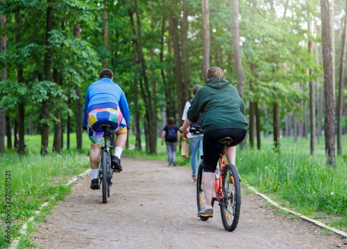 Group of very fat boy and girl friends  riding bikes in a forest. People riding bicycles in the green city park, active Healthy lifestyle . Close up. 