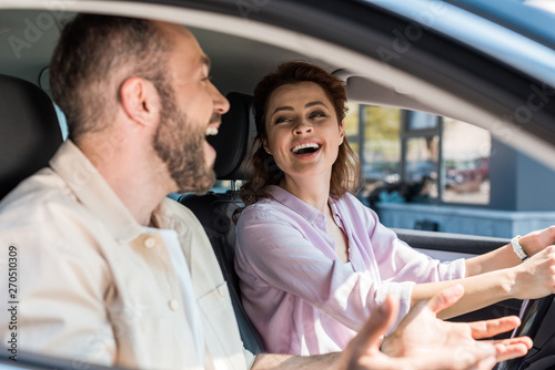 selective focus of cheerful woman looking at happy man gesturing in car