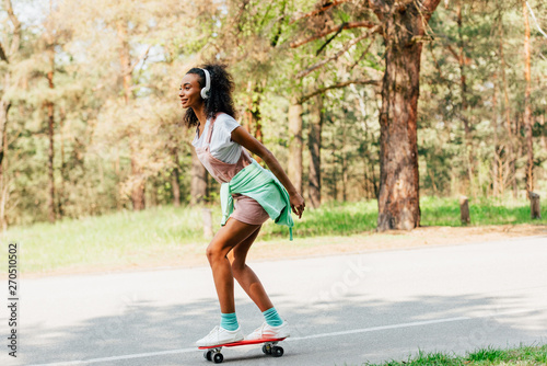 full length view of african american girl skateboarding and listening music in headphones