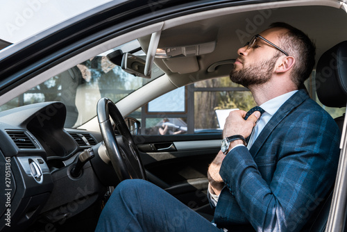 low angle view of bearded businessman in glasses touching tie while sitting in car © LIGHTFIELD STUDIOS