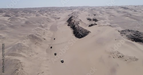 4K high aerial view with beautiful scenery of a convoy of 4x4 vehicles driving between sand dunes and mountains on the Skeleton Coast, Namib desert, Namibia photo