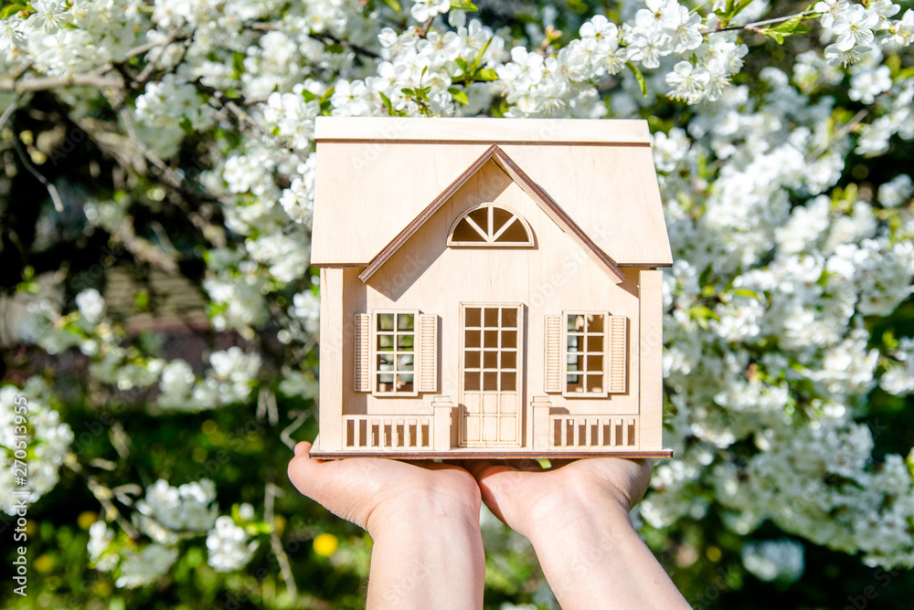 The girl holds the house symbol against the background of blossoming cherry The girl holds the house symbol against the background of blossoming cherry