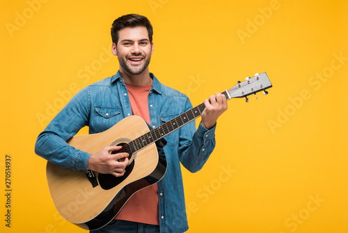 handsome smiling man playing acoustic guitar Isolated On yellow photo