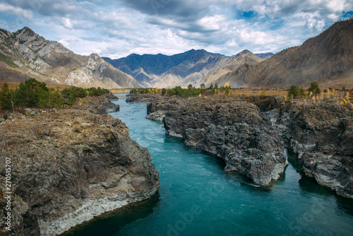 Turquoise Katun river in gorge is surrounded by high mountains under majestic autumn sky. A stormy mountain stream runs among rocks - landscape of the Altai mountains, beautiful places of the planet.
