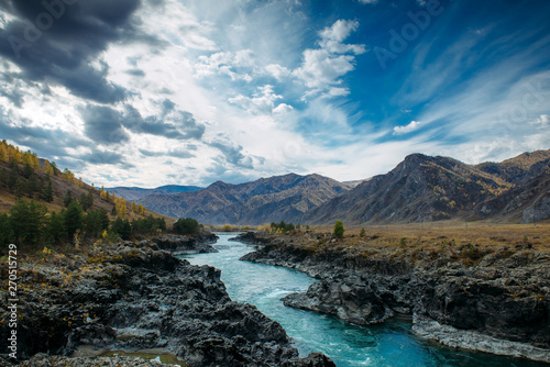 Turquoise Katun river in gorge is surrounded by high mountains under majestic autumn sky. A stormy mountain stream runs among rocks - landscape of the Altai mountains, beautiful places of the planet.