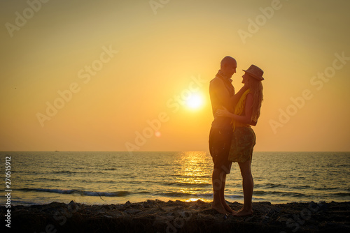 Stylish loving couple hugging each other on the beach at sunset. Man and woman in holiday honeymoon trip.