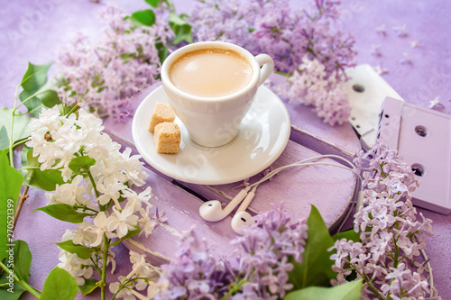 Coffee with cream and cane sugar on a lilac table  surrounded by lilac flowers. Old music cassettes and headphones.