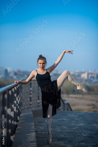 Ballerina in a tutu posing standing by the fence. Beautiful young woman in black dress and pointe dancing outside. Gorgeous ballerina performing a dance outdoors