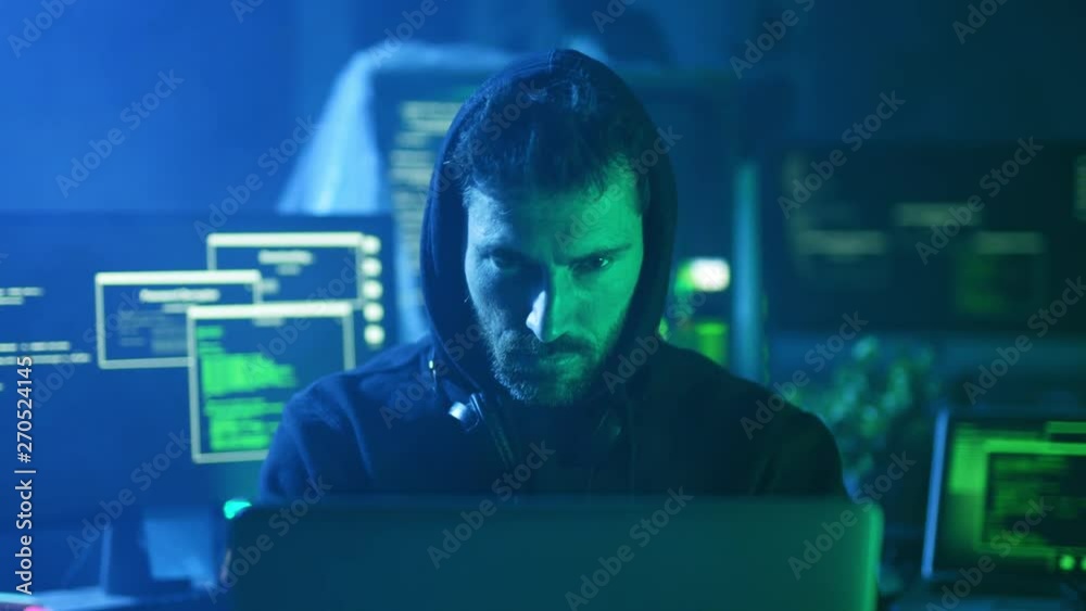 Portrait of dangerous computer hacker working on computer scheming cyber attack on server in the office at night.