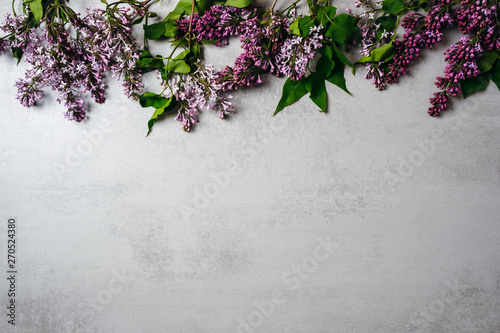 Flower frame of purple lilac bunch on concrete stone surface background. Flat lay, top view, minimal style concept. Greeting card or web banner mockup for wedding anniversary, birthday, womens day.