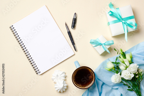 Flat lay women home office desk with coffee cup, blank paper notepad, roses flowers bouquet, gift box and feminine fashion accessories. Top view female workspace, beauty blogger girls desktop.