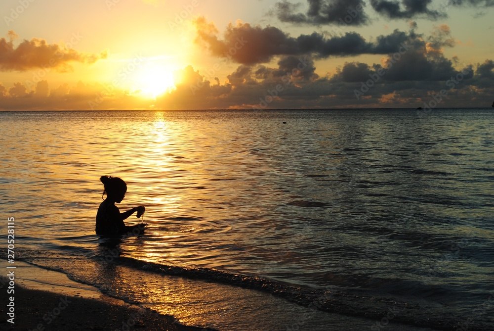 Silhouette of an unrecognizable girl playing with the waves on the beach at sunset, with golden reflections in the water Silhouette of an unrecognizable girl playing with the waves on the beach at sunset, with golden reflections in the water