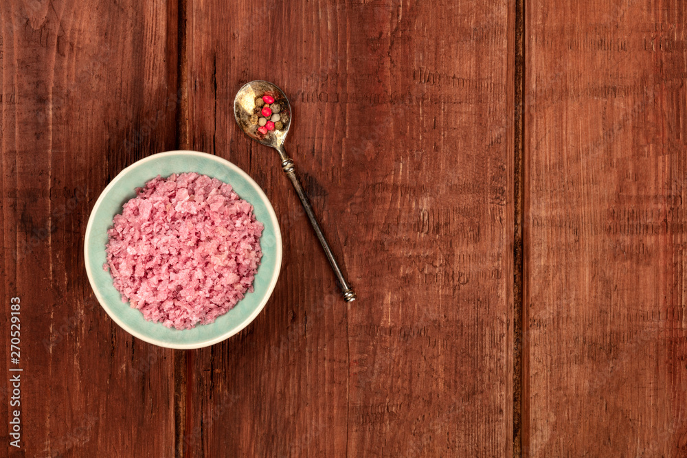 A bowl of pink Himalayan sea salt with pepper, shot from the top on a dark rustic wooden background with a place for text
