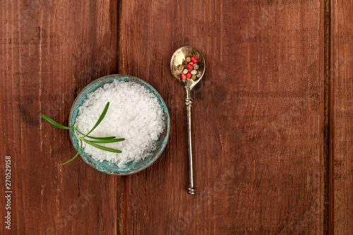 Gourmet spices. Rosemary infused sea salt and a spoon with peppercorns, shot from the top on a dark rustic wooden background with a place for text