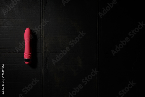 Simple pink dildo on dirty black background with hard light and shadows with copyspace.